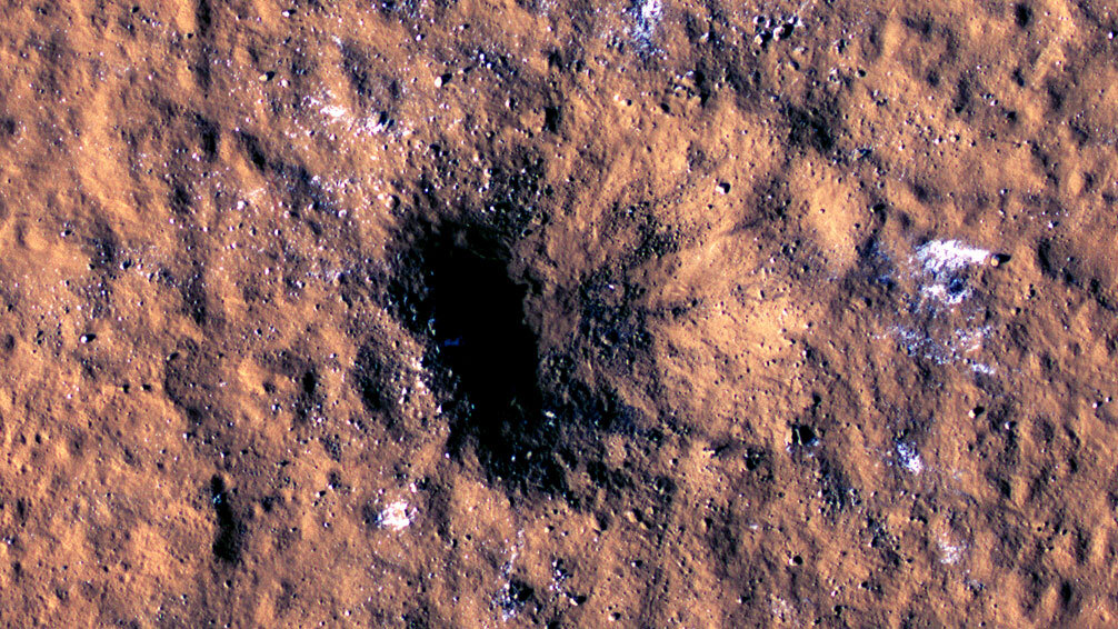 Boulder-size blocks of water ice can be seen around the rim of an impact crater on Mars, as viewed by the High-Resolution Imaging Science Experiment (HiRISE camera) aboard NASA’s Mars Reconnaissance Orbiter. The crater was formed Dec. 24, 2021, by a meteoroid strike in the Amazonis Planitia region.