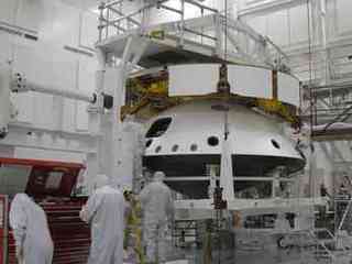 This image shows the cruise structure (the 'ring' on top) and one part of the aeroshell (the backshell with the rover inside) flipped over and the bottom of the aeroshell (the black heat shield) being added.  There are four mission team members in the foreground.