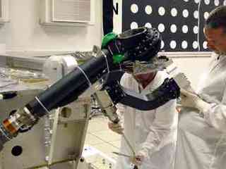 In this image, two technicians from the Mars Science Laboratory team prepare the rover's mobility system for instrumentation tests.  They are both wearing white coats and gloves as they each work on one of the rover's 'legs' in a white-tiled room.