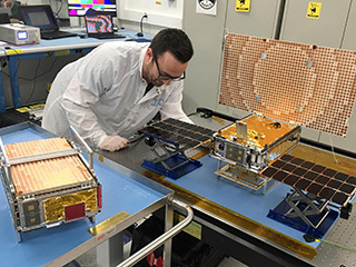 Engineer Joel Steinkraus stands with both of the Mars Cube One (MarCO) spacecraft at NASA's Jet Propulsion Laboratory. 