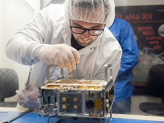 An engineer makes an adjustment on the CubeSat.
