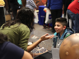 This image shows Amruta Mehta, a member of the Mars InSight Roadshow, speaking with a boy at one of the Roadshow's stops in Santa Maria in May 2018. 