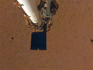An image of InSight's robotic arm, with its scoop and stowed grapple, poised above the Martian soil. The image was received on Dec. 4, 2018 (Sol 8).