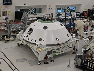 The backshell that will help protect the Mars 2020 rover during its descent into the Martian atmosphere visible in the foreground. A technician on the project monitors the progress of Systems Test 1. 