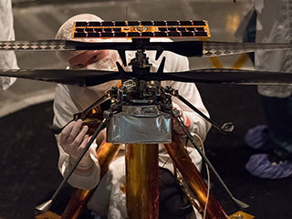 Members of the NASA Mars Helicopter team attach a thermal film to the exterior of the flight model of the Mars Helicopter. 