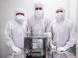 Image of engineers with the Mars 2020 SHERLOC Calibration Target in a clean room at NASA's Johnson Space Center.