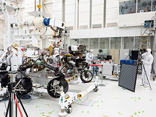In this image, engineers test cameras on the top of the Mars 2020 rover’s mast and front chassis. 
