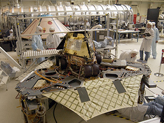 A "Martian mechanic" checks beneath the completely deployed Rover 1 lander. Atop the lander is Rover 1 with its wheels and solar arrays in the stowed position.