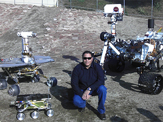 Allen with engineering models of the (clockwise from bottom) Sojourner rover, a Mars Exploration Rover, and Curiosity in JPL's Mars Yard