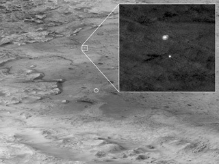 in this image, the descent stage holding NASA’s Perseverance rover can be seen falling thorough the Martian atmosphere, its parachute trailing behind