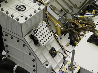 A white, square unit with rows of small color and grayscale dots attached to the top of the Perseverance rover.  