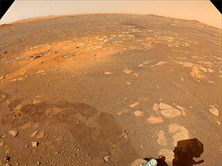 Taken on March 5, 2021, this color-calibrated image from a Navigation Camera aboard NASA’s Mars 2020 Perseverance rover shows tracks from the rover’s first drive (darker marks in the foreground) and an area scoured by the Mars 2020 mission’s descent stage rockets (lighter-colored area in the middle ground). 