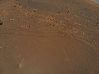 This is a colored image of the sandy surface of Mars. There are small rocks and marks of the rovers wheels on the sandy surface. 