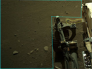 This is an annotated image of Perseverance's robotic arm and an outlined area in AI4Mars. The rover is positioned to the right and wheel tracks and the rocky, sandy surface of Mars are visible in the background. 