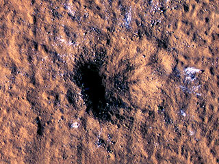 Boulder-size blocks of water ice can be seen around the rim of an impact crater on Mars, as viewed by the High-Resolution Imaging Science Experiment (HiRISE camera) aboard NASA’s Mars Reconnaissance Orbiter. 