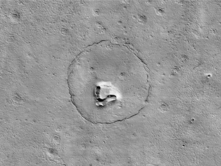 This image taken in December 2022 by HiRISE on MRO appears to show a bear's face on the Mars' surface, made up of a hill, craters and a circular fracture pattern.