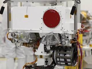 This image shows a close-up of the rover's "head."  At the top is a white box structure with a large red circle (the rover's laser called ChemCam) to the right.  Beneath the box are two cameras, which will provide views of the Martian surface.  They are covered with protective silvery material.