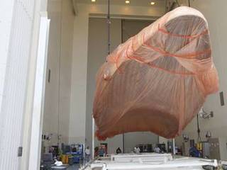 Half of the Atlas V payload fairing for NASA's Mars Science Laboratory (MSL) mission, encased in plastic, is lifted from its transportation pallet in the airlock of the Payload Hazardous Servicing Facility at NASA's Kennedy Space Center in Florida.