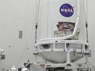 In the Payload Hazardous Servicing Facility at NASA's Kennedy Space Center in Florida, technicians assist as the payload fairing of an Atlas V rocket approaches a transporter for the move to Space Launch Complex 41.
