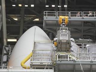 Employees gathered one level above monitor the progress of the protective mesh container known as the "gorilla cage," holding the multi-mission radioisotope thermoelectric generator (MMRTG) for NASA's Mars Science Laboratory (MSL) mission, as it is lifted near the top of the Atlas V rocket in the Vertical Integration Facility at Space Launch Complex 41.
