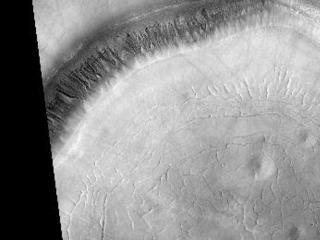 HiRISE image (PSP_001942_2310) shows a crater approximately 11 km (7 miles) in diameter, located in Acidalia Planitia, part of the Northern Plains. Several features in and around this crater are suggestive of fluids and ice at and near the surface. 

The south-looking (or equator facing) walls of this crater are cut by numerous gullies such as the ones shown in this image's cutout (500 x 600 m or 550 x 650 yards), with well developed alcoves, sinuous channels, and terminal fan deposits. These gullies seem to originate at the same height, suggesting that the carving agent may have emanated from one single layer exposed in the crater's wall. 

Contrastingly, no gullies are observed in the north-looking (or pole facing) wall of this crater. Terrestrial gullies very similar to the ones shown in this image are produced by surface water. The arrows in the cutout show fissures that may indicate detachment of surficial materials possibly held together by subsurface ice, sliding en masse down the crater's wall. 

The muted topography of the crater and its surroundings, the relatively shallow floor (300 m or 330 yards), the convex slope of its walls-all are consistent with ice being present under the surface, mixed with rocks and soil. Ice would have acted as a lubricant, facilitating the flow of rocks and soils and hence smoothing landscape's features such as ridges and craters' rims.

The concentric and radial fissures in the crater's floor may indicate decrease of volume due to loss of underground ice. Piles of rocks aligned along these fissures and arranged forming polygons are similar to features observed in terrestrial periglacial regions such as Antarctica. Antarctica's features are produced by repeated expansion and contraction of subsurface soil and ice, due to seasonal temperature oscillations. The funnel-shaped depressions visible in the crater's floor could be collapse pits, further evidence of ice decay; alternatively, they could be smoothed-out impact craters.