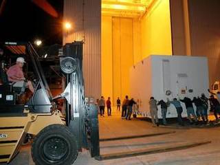 Workers roll one of two containers with the Mars Reconnaissance Orbiter equipment into the Payload Hazardous Servicing Facility, Kennedy Space Center.