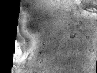 This image is located near the boundary between Syrtis Major and Isidis Planitia. The top of the image shows rough material that has eroded away from the lower portion of the image, revealing an underlying surface that has many small craters. It also reveals an ancient flow lobe that is barely discernable, crossing the southern part of the image (this flow lobe is much easier to see as a smooth region in the context image).