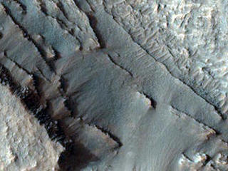 This image shows part of the floor of an impact crater on the northern rim of the giant Hellas Basin. 

Hellas includes the lowest elevations on Mars, and may have once held lakes or seas; layered rock outcrops occur around much of the edge of the basin. At this site, a large impact crater (about 90 kilometers across) was partly filled by layered rocks. These rocks on the crater floor are now eroding and forming strange pits.

Here, the layers are mostly exposed on a steep slope which cuts across much of the image. On this slope, they crop out as rocky stripes, some continuous and others not. The material between the stripes is mostly covered by debris, but some areas of exposed rock are visible. The slope is capped by a thick, continuous layer that armors it against erosion; once this cap is gone, the lower material is removed rapidly, forming the steep slope. At the base of this slope, rocks on the floor of the pit appear bright and heavily fragmented by cracks known as joints.

The variation in rock types suggests that the rocks here were deposited by multiple processes or in different environments. Sites like this may preserve a record of conditions on early Mars.