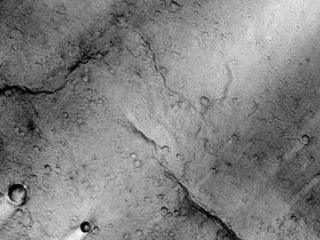 This image is near the southern edge of a low, broad volcanic feature called Syrtis Major. A close look at this image reveals a wrinkly texture that indicates a very rough surface that is associated with the lava flows that cover this region. On a larger scale, there are numerous bright streaks that trail topographic features such as craters. These bright streaks are in the wind shadows of the craters where dust that settles onto the surface is not as easily scoured away. It is important to note that these streaks are only bright in a relative sense to the surrounding image. Syrtis Major is one of the darkest regions on Mars and it is as dark as fresh basalt flows or dunes are on Earth.