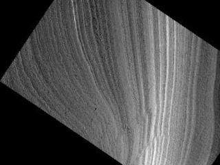 This image shows an outcrop of the south polar layered deposits (SPLD). The SPLD consist of layers of ice and admixed dust and make up the bulk of the dome-shaped Planum Australe.

Planum Australe is, in some ways, analogous to the Antarctic ice sheet. Troughs and scarps carved into Planum Australe by erosional processes have exposed SPLD layers within it. In this image, the darkest area at the bottom of the image is the bottom of the scarp. Except for the dark material at the bottom of the slope, much of the changes in brightness in this image are due to the lighting angle, the direction from which the sun is illuminating the slope.

Much like ice cores from Greenland and Antarctica and deep sea sediment cores, the icy-dusty layers of the SPLD may have preserved a record of recent Mars climate history. Understanding that record is a complex process and involves, among many other types of analyses, examining the differences and similarities in appearance between each layer and attempting to classify layer types. This image shows nice examples of different layer textures. But what is especially interesting about this image are the faults cutting through the layers. These faults appear as diagonal lines, on either side of which, the layering is offset. Note that the faults are not clean, single lines, but appear in long groups of short lines.

What caused these faults is still under investigation, but, among other possibilities, they could be related to an earlier time when temperatures were higher and the ice was flowing at a much faster rate than it is today.