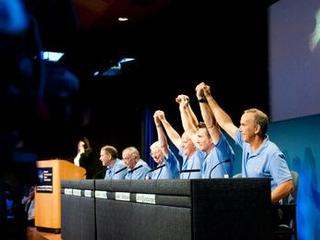 Mars Science Laboratory mission scientists, flight controllers, managers and administrators raise their hands to a cheering crowd at a news conference following the successful landing of NASA's Curiosity rover on Mars.