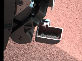 In this image, the scoop on NASA's Curiosity rover shows the larger soil particles that were too big to filter through a sample-processing sieve that is porous only to particles less than 0.006 inches (150 microns) across.