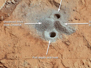 This image shows the first holes into rock drilled by NASA's Mars rover Curiosity, with drill tailings around the holes plus piles of powdered rock collected from the deeper hole and later discarded after other portions of the sample had been delivered to analytical instruments inside the rover.