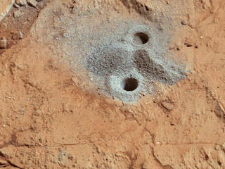 This image shows the first holes into rock drilled by NASA's Mars rover Curiosity, with drill tailings around the holes plus piles of powdered rock collected from the deeper hole and later discarded after other portions of the sample had been delivered to analytical instruments inside the rover.