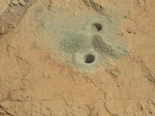 This image shows the first holes into rock drilled by NASA's Mars rover Curiosity, with drill tailings around the holes plus piles of powdered rock collected from the deeper hole and later discarded after other portions of the sample had been delivered to analytical instruments inside the rover.