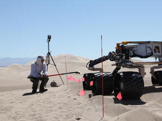sand dune, mars rover, wheel, Dumont, Scarecrow, test - This image shows the scarecrow test rover going over a dunes obstacle course, while an engineer hunches down to see the wheels as it drives.
