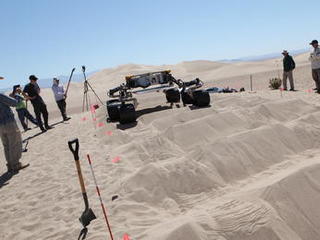 sand dune, mars rover, wheel, Dumont, Scarecrow, test - Several engineers flank the Scarecrow mobility rover on both sides as the rover drives over a sand dunes obstacle course.