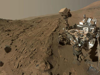 Curiosity, rover, self-portrait, rock, drilling, windjana, waypoint, kimberley - This image is a self-portrait of the Curiosity rover taken from the site with the rover's 'head' down, with rock formations surrounding it and Mount Sharp in the background.