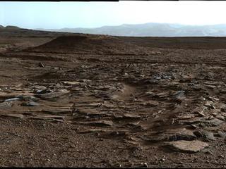 This April 4, 2014, image from Curiosity's Mastcam looks to the west of a waypoint on the rover's route to Mount Sharp. The mountain lies to the left of the scene. The image shows sets of sandstone beds inclined to the south (left), indicating progressive build-out of sediment toward Mount Sharp.