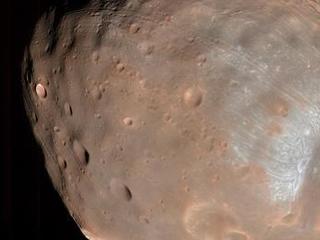 This is a color image of the largest of Mars' two moons, Phobos.  It appears pinkish in color with a giant crater dent on the far, right-side.  The crater edges seem whiter than the rest of the image.
