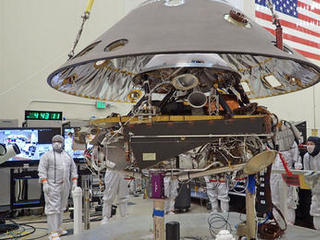 In this photo, the back shell of NASA's InSight spacecraft is being lowered onto the mission's lander, which is folded into its stowed configuration.