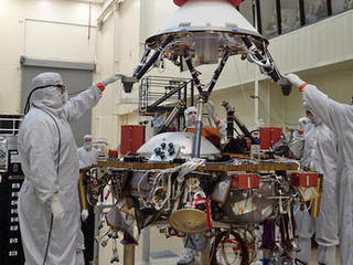 In this photo, spacecraft specialists at Lockheed Martin Space Systems, Denver, are reaching up to guide lowering of the parachute cone for installation onto NASA's InSight spacecraft.