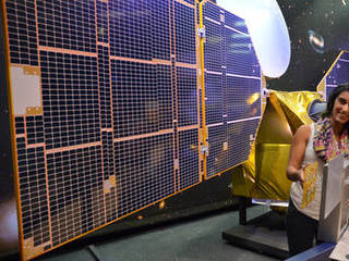 The full-scale mock-up of NASA's MarCO CubeSat held by Farah Alibay, a systems engineer at NASA's Jet Propulsion Laboratory, is dwarfed by the one-half-scale model of NASA's Mars Reconnaissance Orbiter behind her.