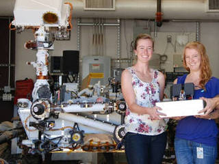 JPL researchers Jessica Creamer, Fernanda Mora and Peter Willis (left to right) pose with the Chemical Laptop, a device designed to detect amino acids and fatty acids. At left is a near-identical copy of the Curiosity rover, which has been on Mars since 2012.