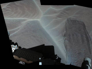 NASA's Mars Curiosity rover looks down on its wheel track, revealing sand grains beneath the surface of a shallow, rippled sand dune.