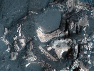 This image shows blocks of bright, layered rock embedded in darker material that are thought to have been deposited by a giant flood that occurred when Uzboi Valles breached the rim of Holden Crater.