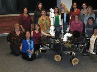 This photo shows fifteen of the women engineers and scientists who work on the Mars Exploration Rover. They are standing behind or kneeling beside a precise replica of the rover in the mission control room.